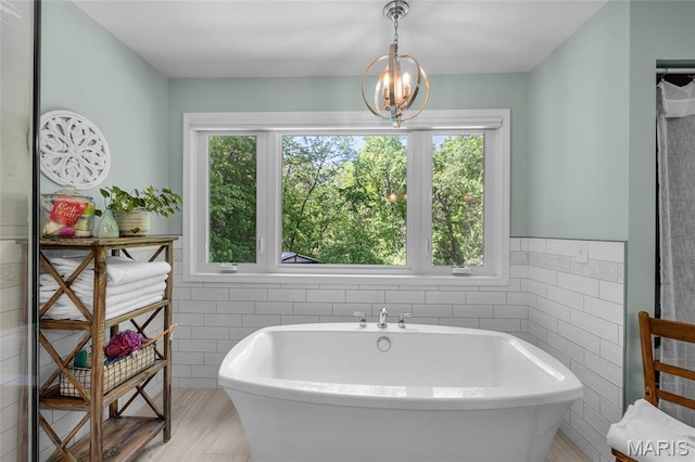 bathroom featuring tile walls, a freestanding tub, and a chandelier