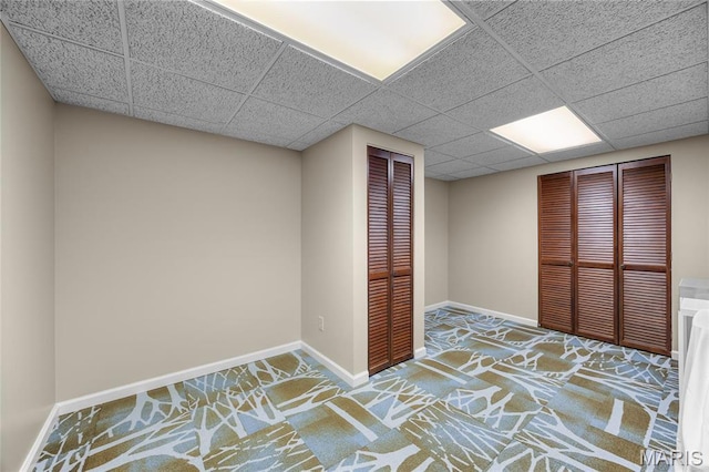 unfurnished bedroom featuring carpet floors, a drop ceiling, and baseboards