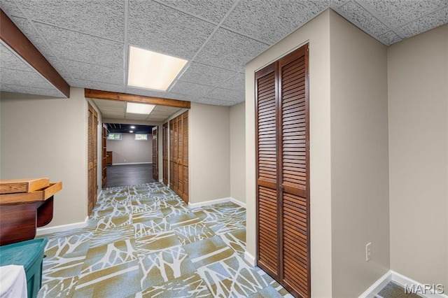 hallway with a paneled ceiling and baseboards