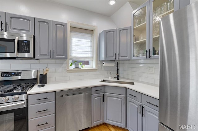 5245 Robert Ave, Saint Louis, MO 63109 - kitchen featuring stainless steel appliances, gray cabinetry, a sink, tasteful backsplash, and glass insert cabinets