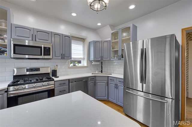 5245 Robert Ave, Saint Louis, MO 63109 - kitchen featuring appliances with stainless steel finishes, gray cabinetry, a sink, glass insert cabinets, and decorative backsplash
