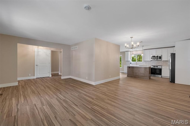 1200 Auber Dr, Manchester, MO 63011 - unfurnished living room with light wood finished floors, a chandelier, and baseboards