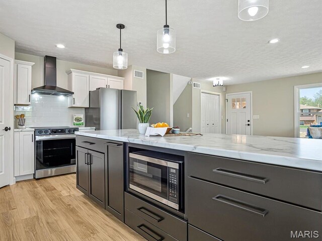 496 E 2nd St, Trenton, IL 62293 - kitchen featuring appliances with stainless steel finishes, wall chimney exhaust hood, light wood-type flooring, white cabinets, and pendant lighting