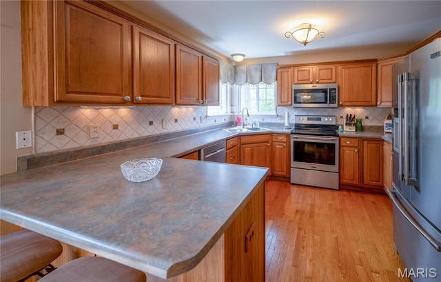 1004 Kodiak Ct, Wentzville, MO 63385 - kitchen with stainless steel appliances, a peninsula, brown cabinets, a kitchen breakfast bar, and light wood-style flooring