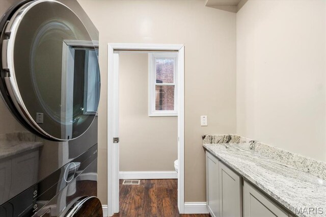 5518 Alaska Ave, Saint Louis, MO 63111 - laundry room with dark wood-style flooring, stacked washer and clothes dryer, and baseboards