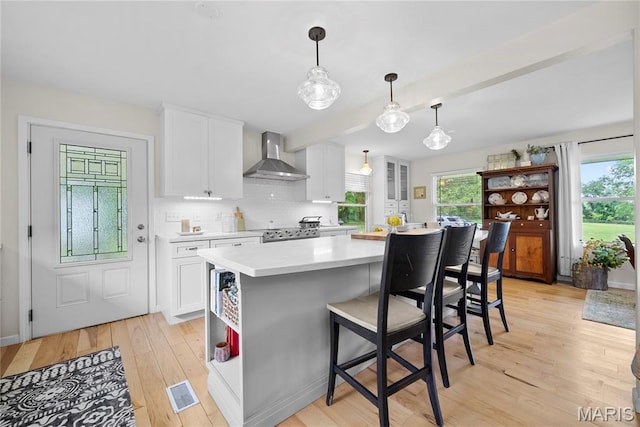 3066 W Meyer Rd, Foristell, MO 63348 - kitchen with wall chimney range hood, light countertops, white cabinetry, light wood-style flooring, and a kitchen breakfast bar