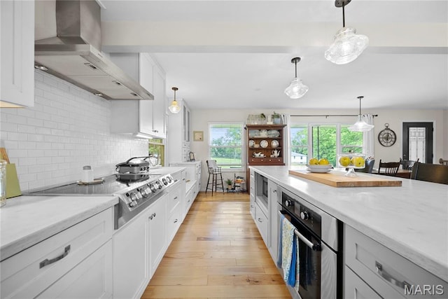 3066 W Meyer Rd, Foristell, MO 63348 - kitchen featuring wall chimney range hood, stainless steel appliances, white cabinetry, tasteful backsplash, and light wood finished floors