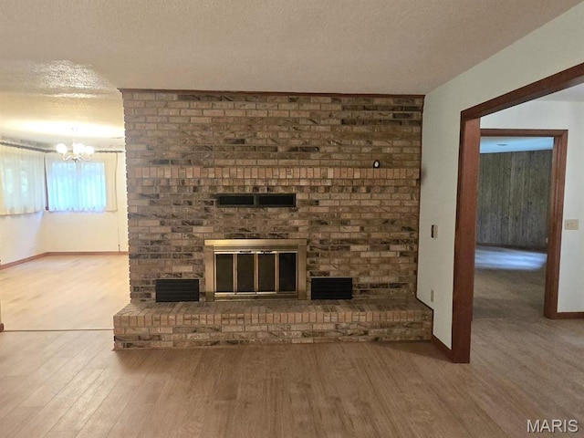16043 County Road 624, Dexter, MO 63841 - unfurnished living room featuring wood finished floors, a chandelier, a brick fireplace, a textured ceiling, and baseboards