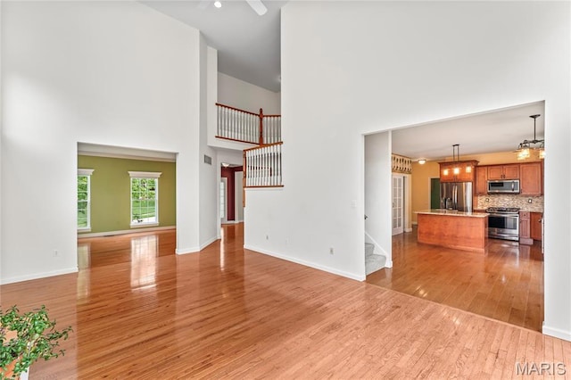 2158 Avalon Ridge Cir, Fenton, MO 63026 - unfurnished living room featuring a high ceiling, stairway, light wood-type flooring, a ceiling fan, and baseboards