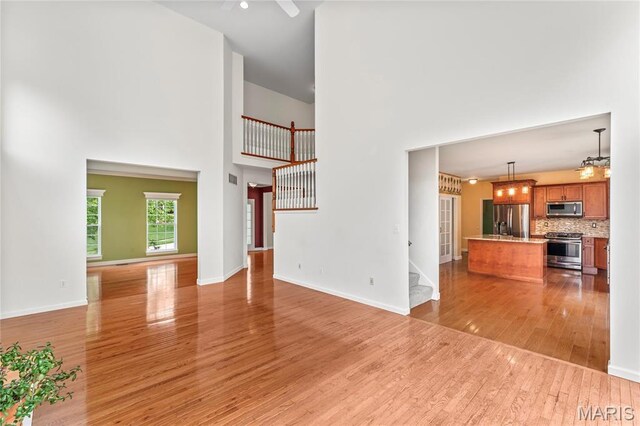 2158 Avalon Ridge Cir, Fenton, MO 63026 - unfurnished living room featuring a high ceiling, stairway, light wood-style flooring, ceiling fan, and baseboards