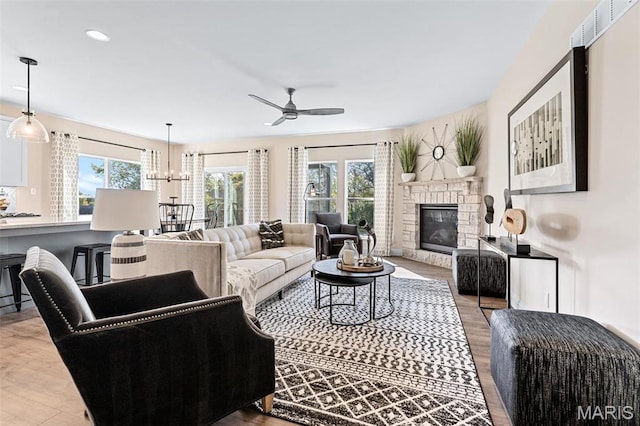living room with wood finished floors, a ceiling fan, a stone fireplace, and recessed lighting