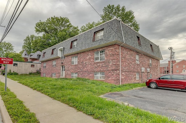 view of home's exterior with mansard roof, roof with shingles, brick siding, and a yard