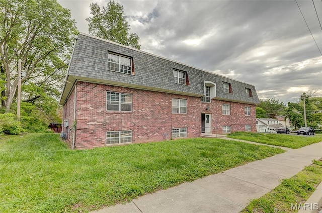 view of front of home featuring mansard roof, roof with shingles, brick siding, and a front yard