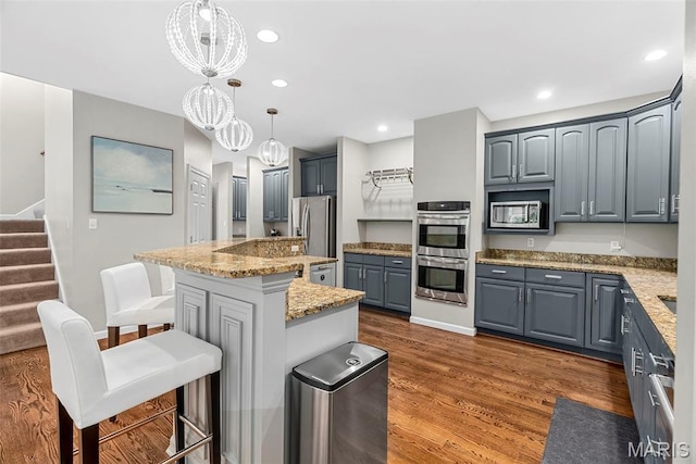 1424 Haarman Oak Dr, Wildwood, MO 63005 - kitchen with appliances with stainless steel finishes, a kitchen bar, dark wood finished floors, light stone countertops, and a center island