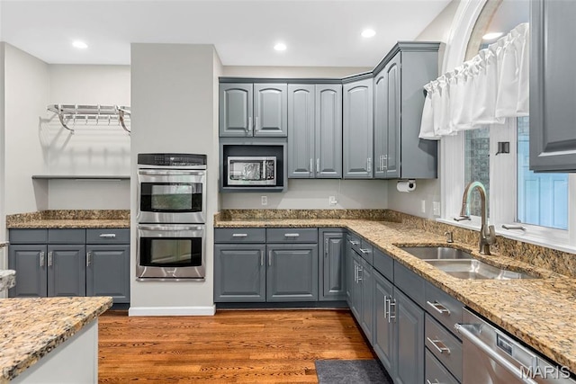1424 Haarman Oak Dr, Wildwood, MO 63005 - kitchen with stainless steel appliances, a sink, wood finished floors, gray cabinetry, and light stone counters