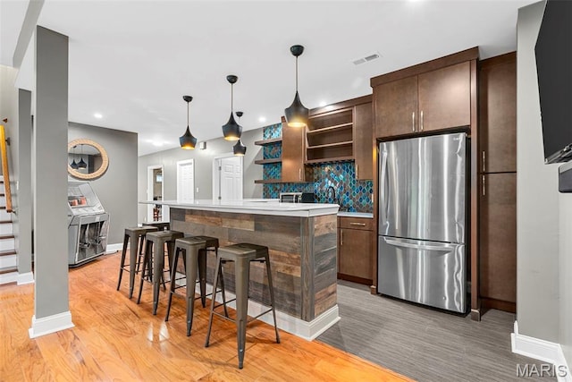 1424 Haarman Oak Dr, Wildwood, MO 63005 - kitchen featuring freestanding refrigerator, open shelves, dark brown cabinetry, tasteful backsplash, and a kitchen bar
