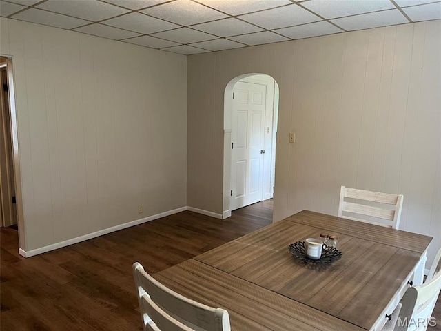 dining space with arched walkways, wood finished floors, baseboards, and a drop ceiling