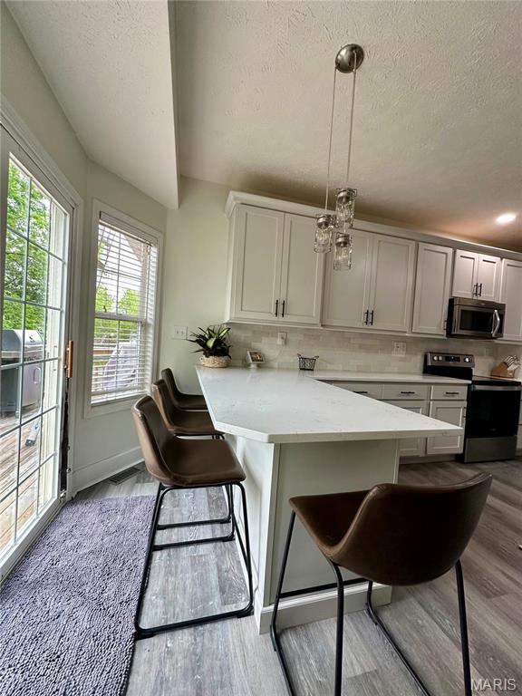 1324 Chelsea Ln, Rolla, MO 65401 - kitchen with stainless steel appliances, a textured ceiling, a kitchen breakfast bar, light wood finished floors, and light countertops