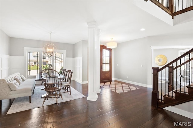 dining room with healthy amount of natural light, stairway, decorative columns, wood finished floors, and a decorative wall