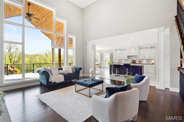 living room featuring dark wood-style floors, a high ceiling, ceiling fan, decorative columns, and baseboards
