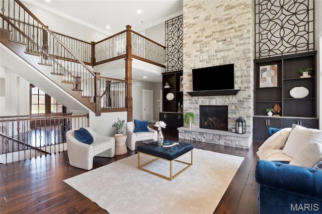 living room featuring dark wood-type flooring, crown molding, a stone fireplace, a towering ceiling, and recessed lighting