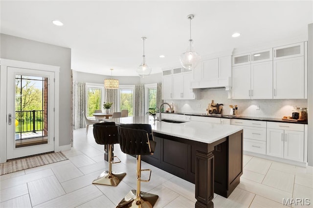 kitchen featuring a sink, decorative backsplash, a kitchen island with sink, white cabinetry, and glass insert cabinets
