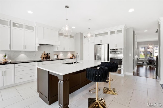 kitchen with a sink, stainless steel appliances, a kitchen breakfast bar, backsplash, and a kitchen island with sink