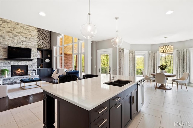 kitchen featuring a sink, stainless steel dishwasher, decorative light fixtures, a fireplace, and light stone counters