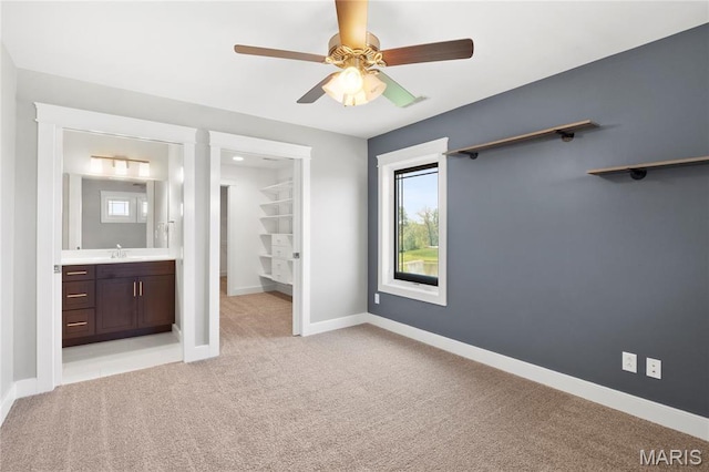 unfurnished bedroom featuring a walk in closet, a sink, light carpet, and baseboards
