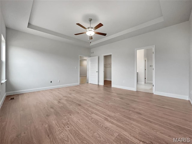 130 Stone Canyon Blvd, Foristell, MO 63348 - unfurnished bedroom featuring a tray ceiling, light wood-style floors, baseboards, and a walk in closet