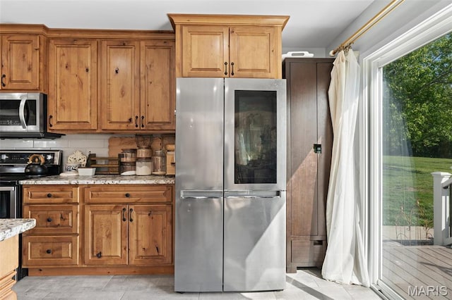 kitchen with appliances with stainless steel finishes, brown cabinetry, decorative backsplash, and light stone counters