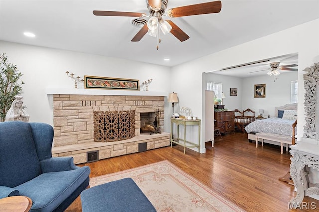 living room with ceiling fan, a stone fireplace, wood finished floors, and recessed lighting