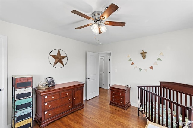 bedroom with wood finished floors, ceiling fan, and a crib