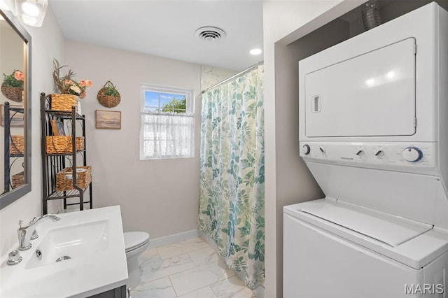 bathroom with stacked washing machine and dryer, marble look tiles, toilet, vanity, and baseboards