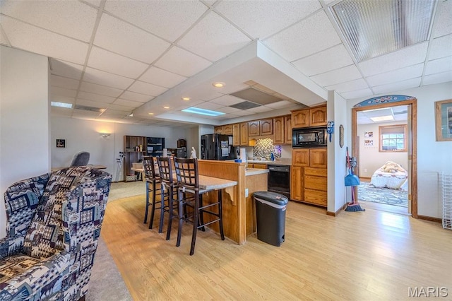 23598 Falcon Rd, Lebanon, MO 65536 - kitchen featuring black appliances, a drop ceiling, light wood finished floors, a breakfast bar, and brown cabinets