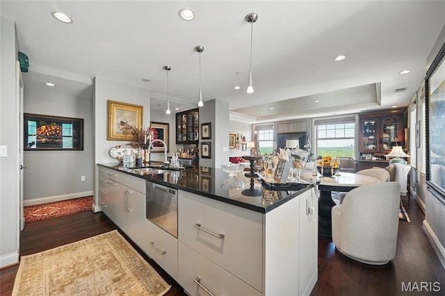 kitchen with a sink, stainless steel dishwasher, open floor plan, dark countertops, and baseboards