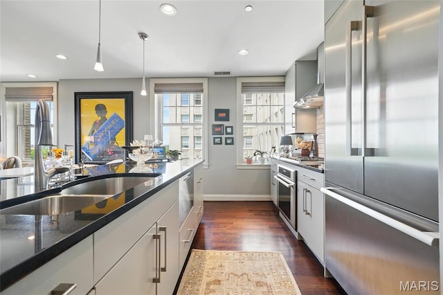 kitchen featuring stainless steel appliances, a sink, baseboards, dark wood-style floors, and dark stone countertops