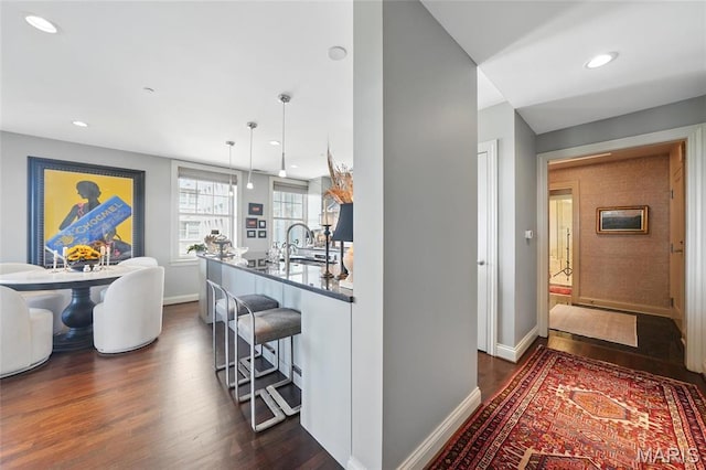 kitchen featuring dark wood-type flooring, a breakfast bar, baseboards, a sink, and recessed lighting