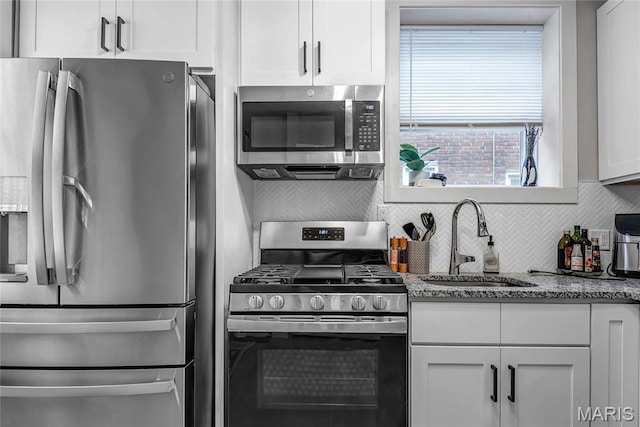 kitchen with appliances with stainless steel finishes, a sink, tasteful backsplash, stone counters, and white cabinets