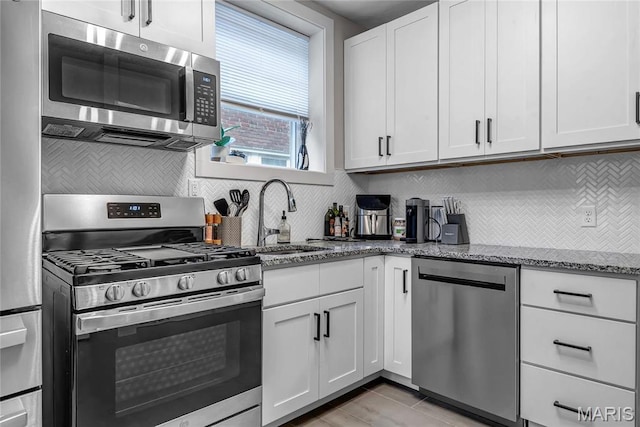 kitchen with stainless steel appliances, a sink, stone counters, white cabinetry, and tasteful backsplash
