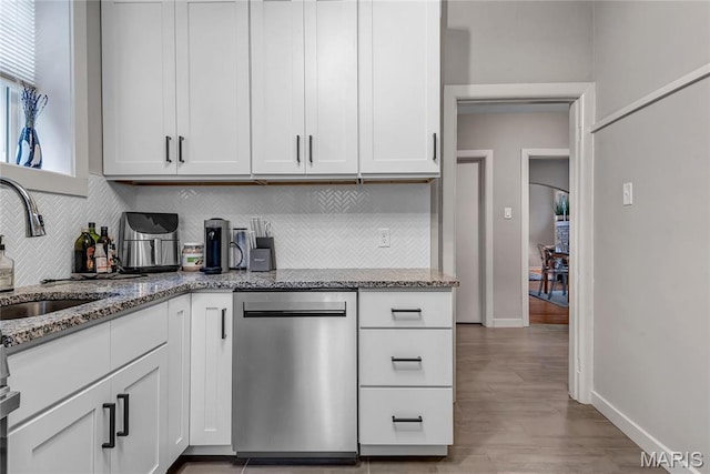 kitchen featuring stainless steel dishwasher, a sink, light stone counters, and backsplash