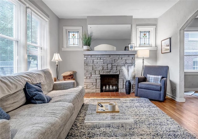 living room with wood finished floors, a stone fireplace, and baseboards