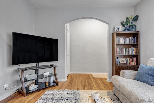 living area featuring arched walkways, wood finished floors, and baseboards