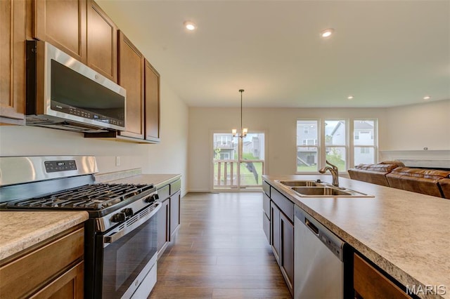 kitchen with stainless steel appliances, a sink, dark wood-style flooring, open floor plan, and hanging light fixtures