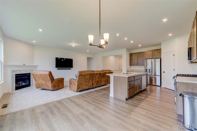 kitchen with stainless steel appliances, open floor plan, a sink, a center island with sink, and light wood-style flooring