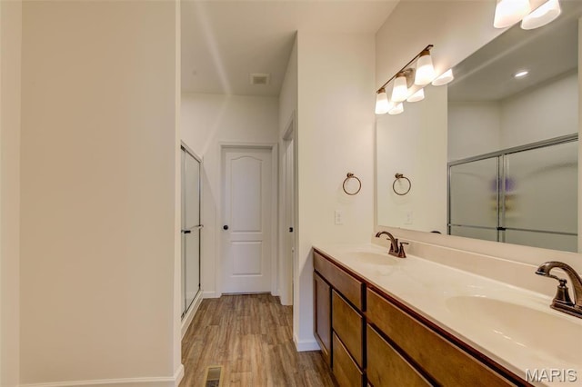 full bathroom with a stall shower, wood finished floors, double vanity, and baseboards