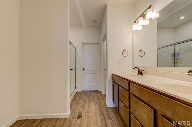 full bath featuring wood finished floors, a shower stall, double vanity, and baseboards