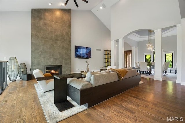 living room featuring high vaulted ceiling, decorative columns, wood finished floors, a ceiling fan, and a tile fireplace