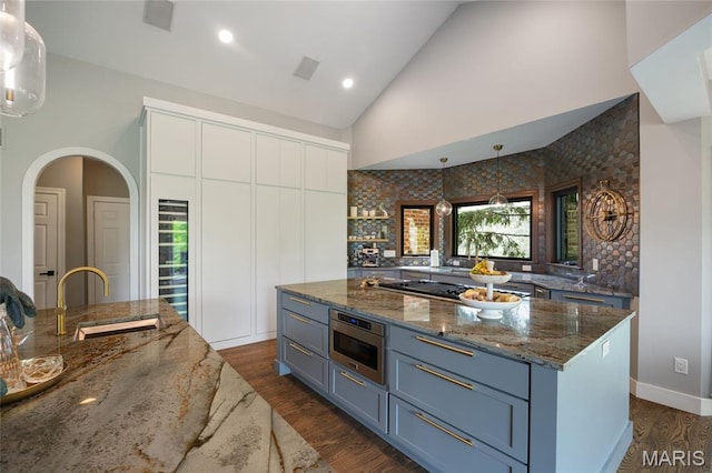 kitchen featuring a sink, stainless steel gas cooktop, high vaulted ceiling, stone counters, and dark wood-style floors