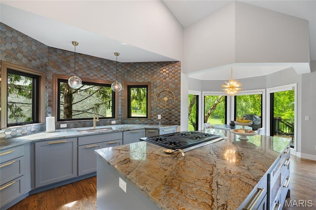 kitchen with a sink, gas cooktop, light stone countertops, high vaulted ceiling, and decorative light fixtures